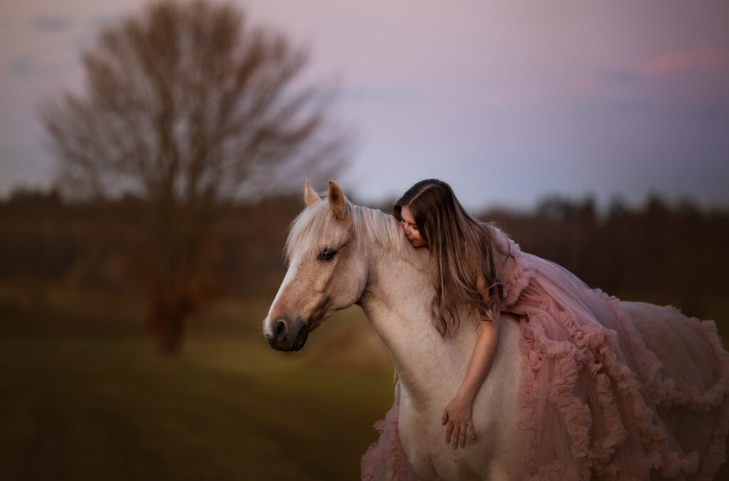 Mädchen in rosa Tüllkleid auf Pferd im Sonnenuntergang