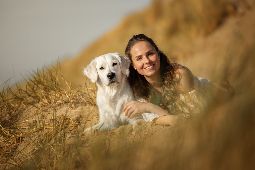 Junge Frau in weißem Kleid kuschelt mit Hund am Strand