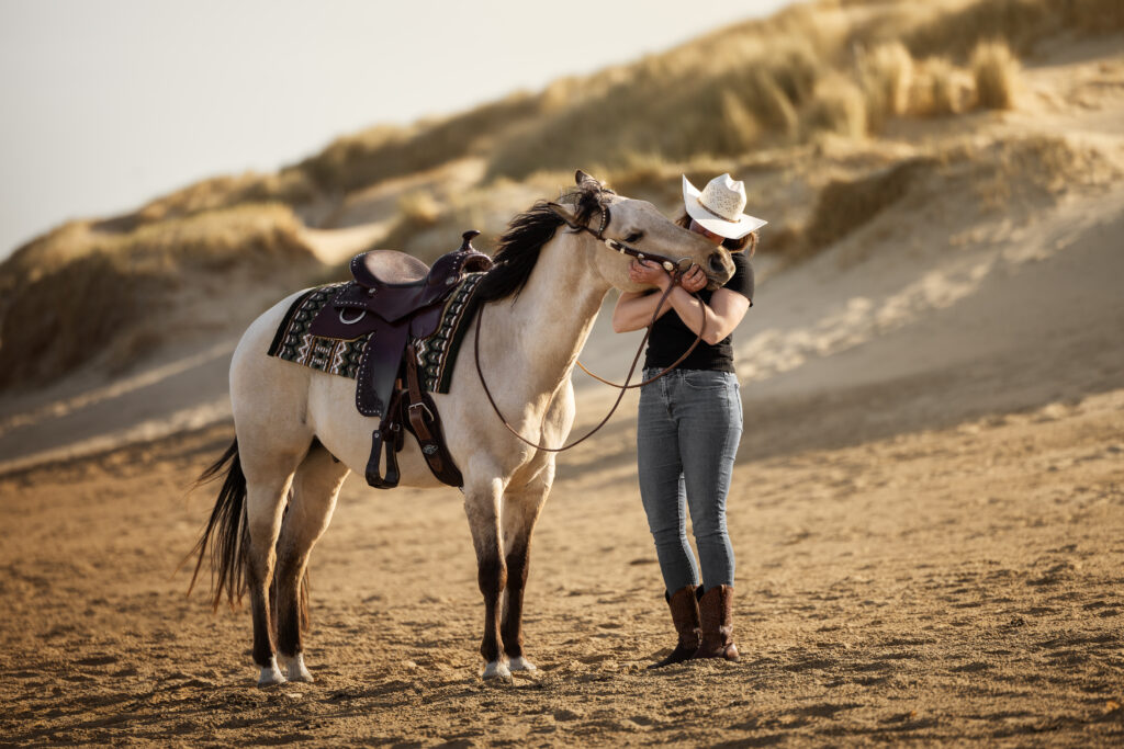 Frau kuschelt mit ihrem Pferd am Strand im Westernoutfit