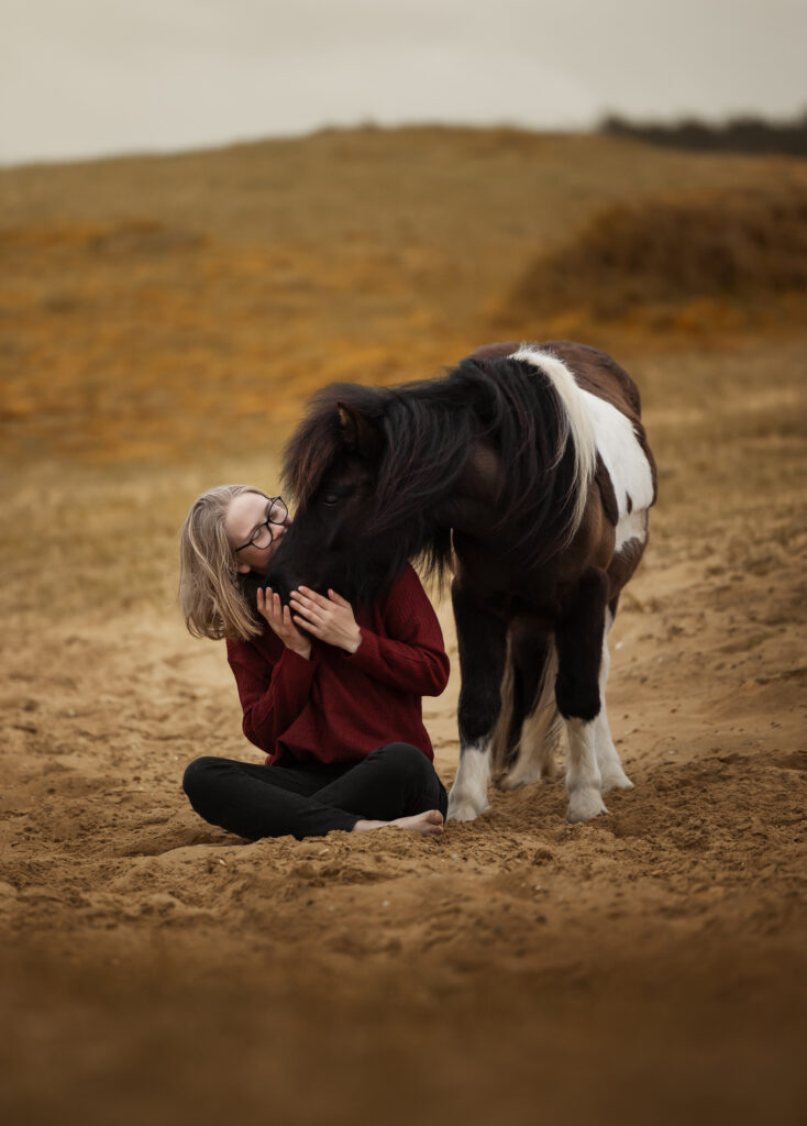 Frau kuschelt mit ihrem Shetland Pony in den Dünen in Holland